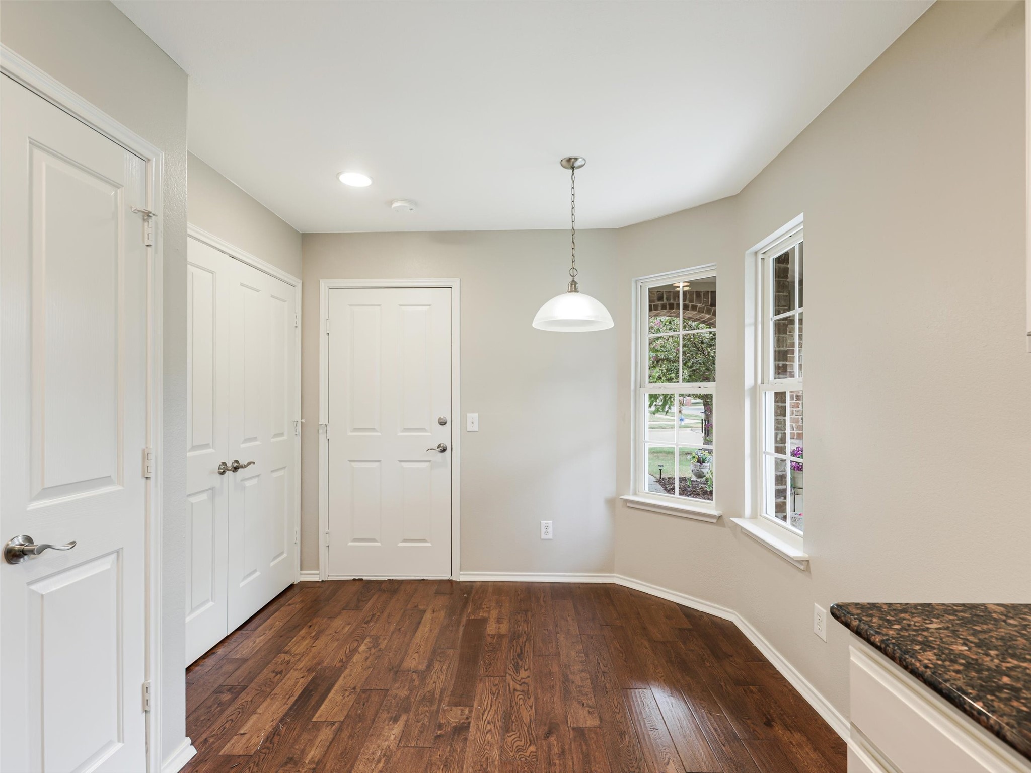 Dining nook with dark hardwood floors, a white pendant light, and two windows.