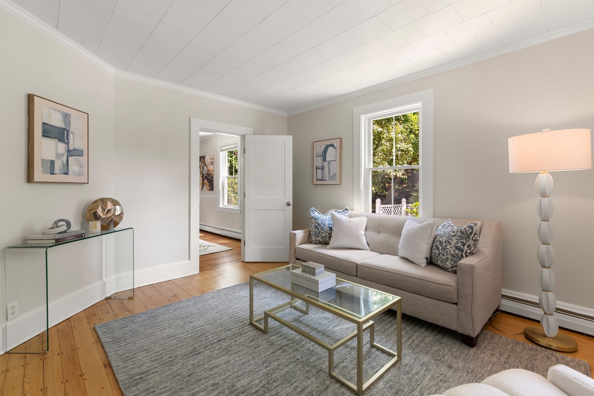 Staged living room with a beige sofa, glass coffee table, and hardwood floors.