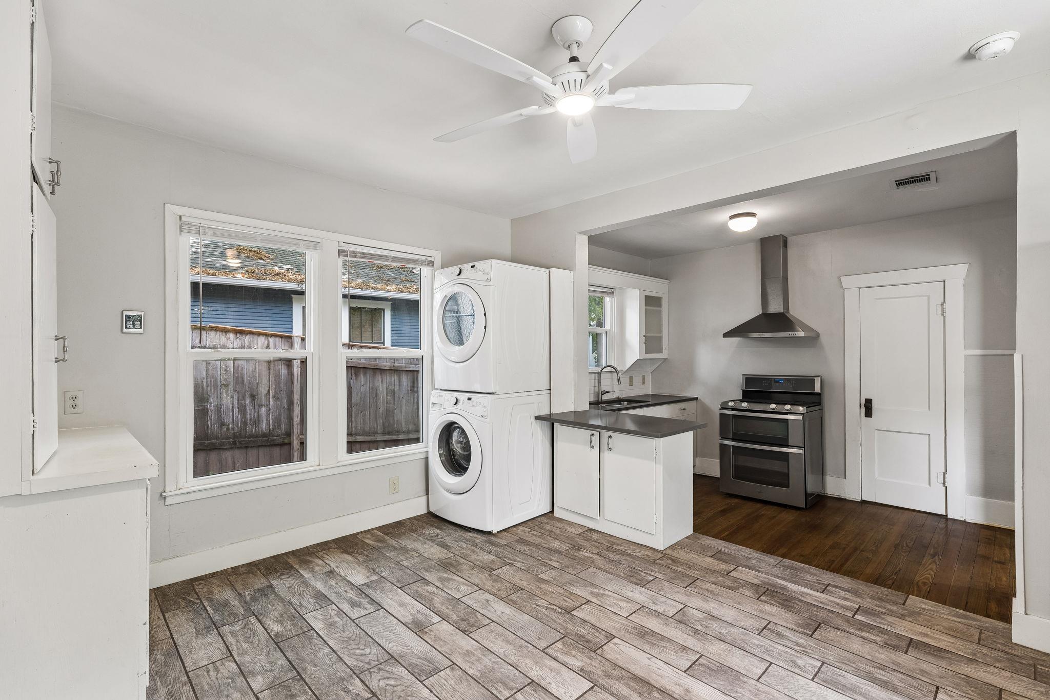 Kitchen with stacked washer and dryer beside two windows, dark countertops, and a stainless range.