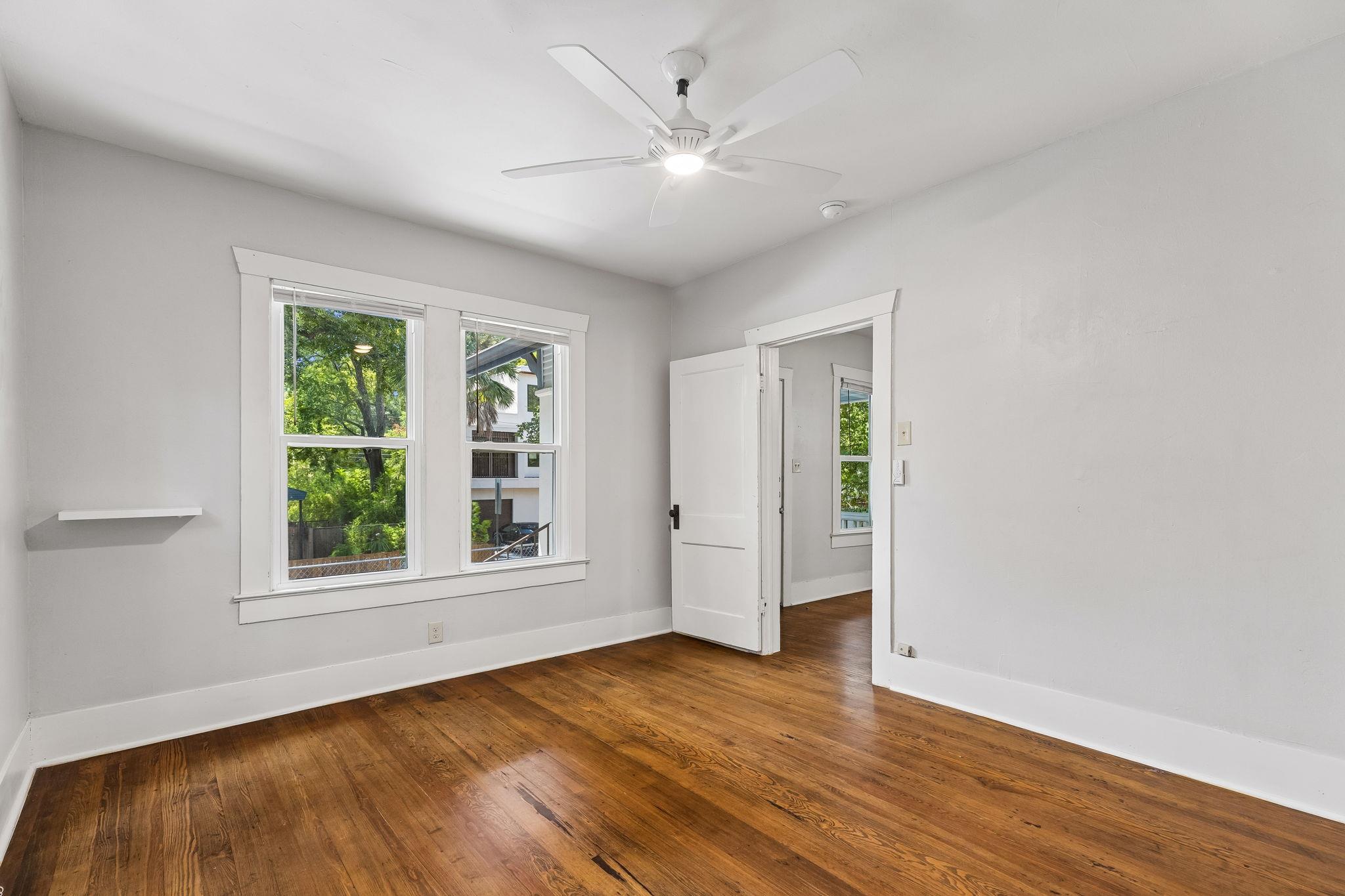 Empty room with hardwood floors, two windows, and a white ceiling fan.
