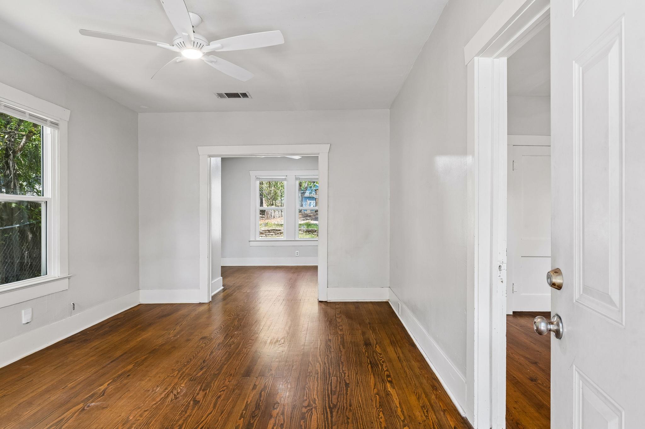 Vacant room with polished hardwood floors, a ceiling fan, and a wide doorway to another room.
