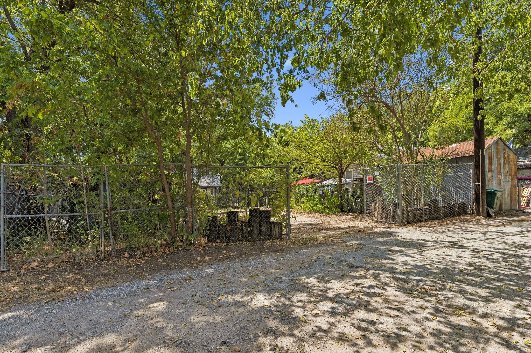 Tree-shaded yard with chain-link fencing, a gravel drive, and a weathered outbuilding.