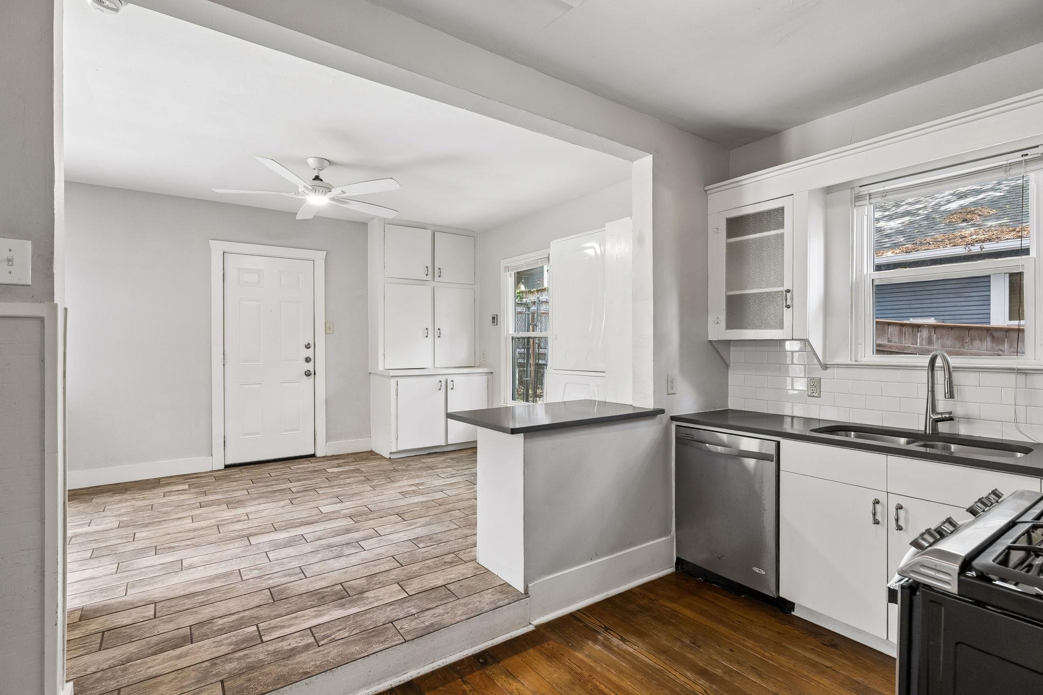Vacant kitchen with a dark-countered peninsula, white cabinets, stainless steel appliances, and adjacent tiled dining area.