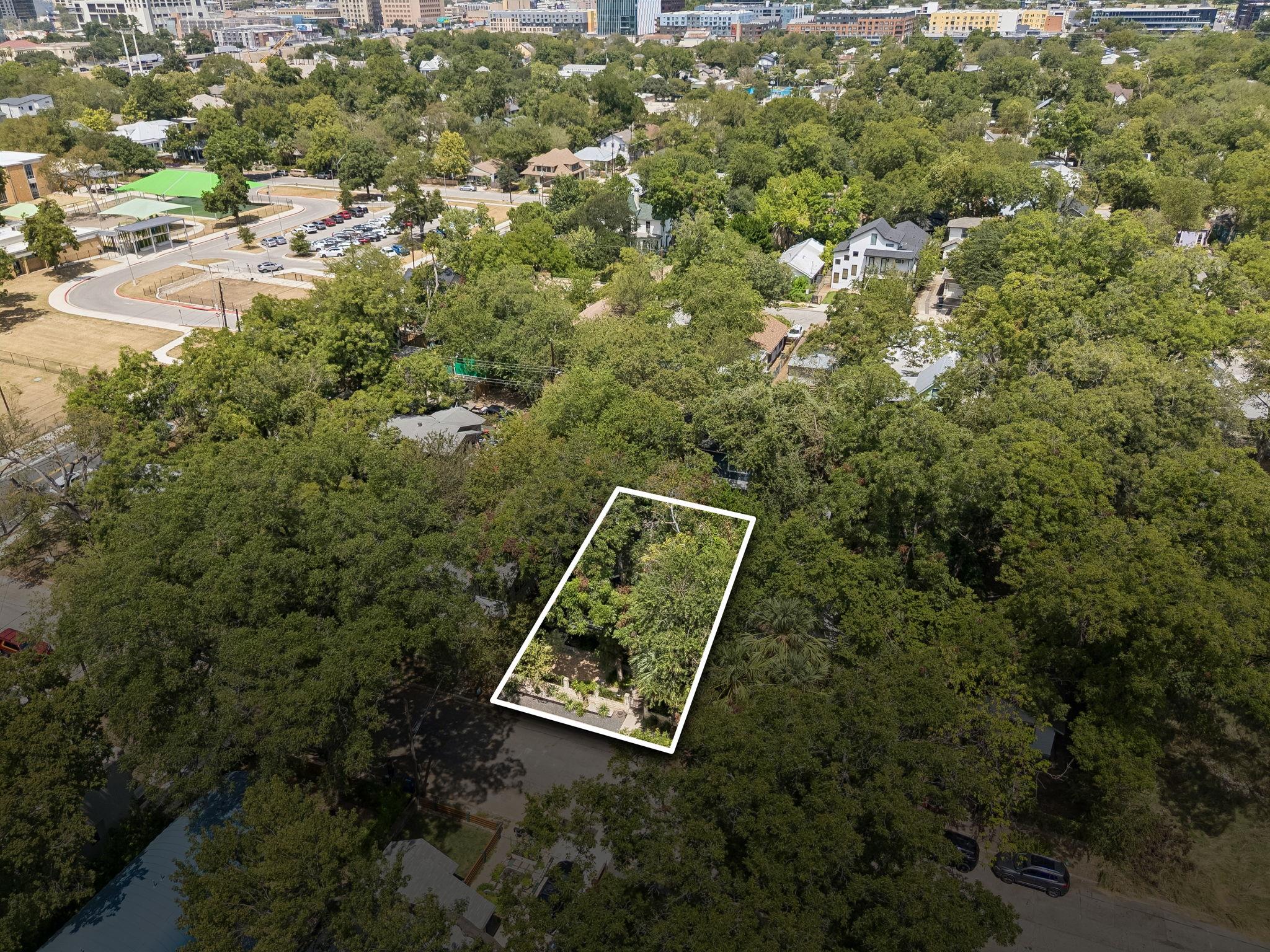 Aerial view of a tree-covered property lot outlined in white amid an Austin neighborhood.