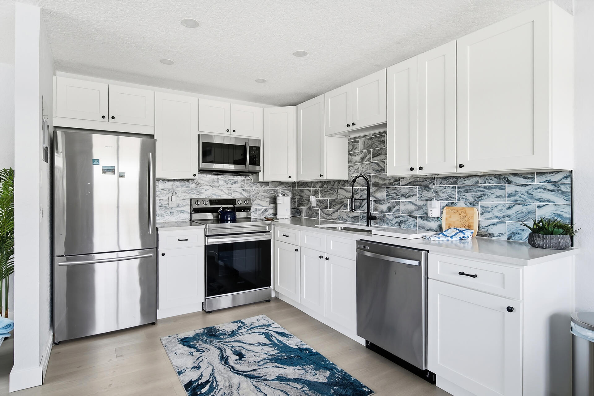 Kitchen with white cabinets, stainless steel appliances, and a blue-gray patterned tile backsplash.
