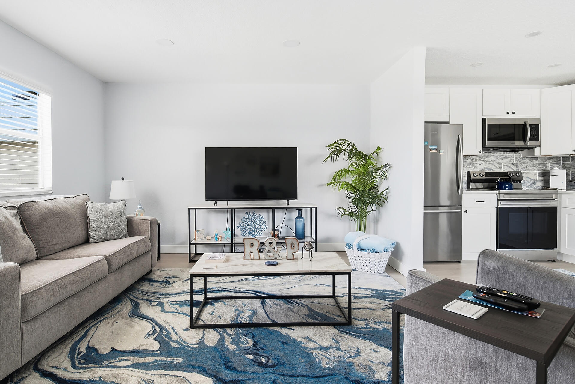 Living room with a gray sectional, television, blue patterned rug, and adjoining white kitchen.