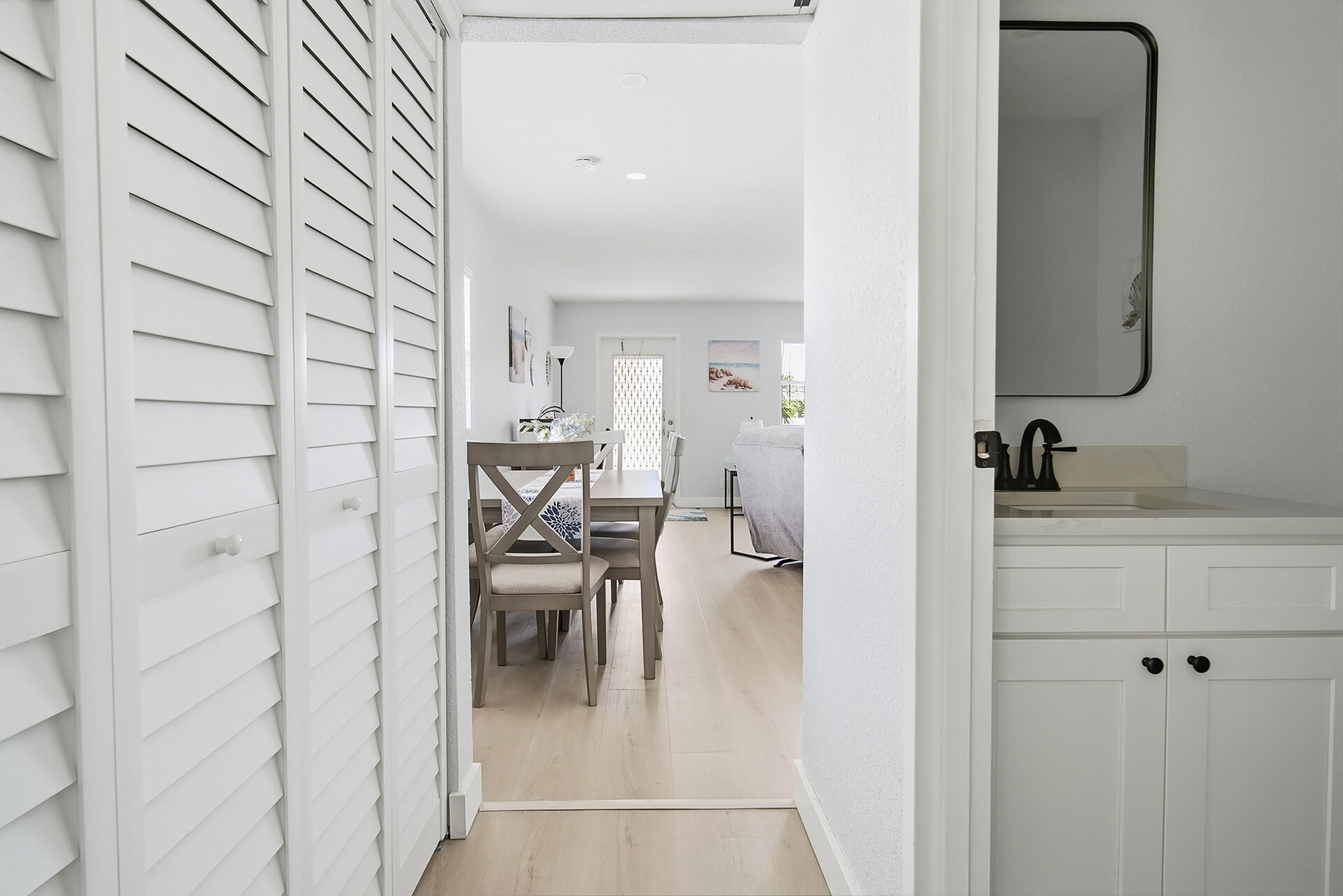 Dining area with a table and chairs, framed by louvered doors and a bathroom vanity.