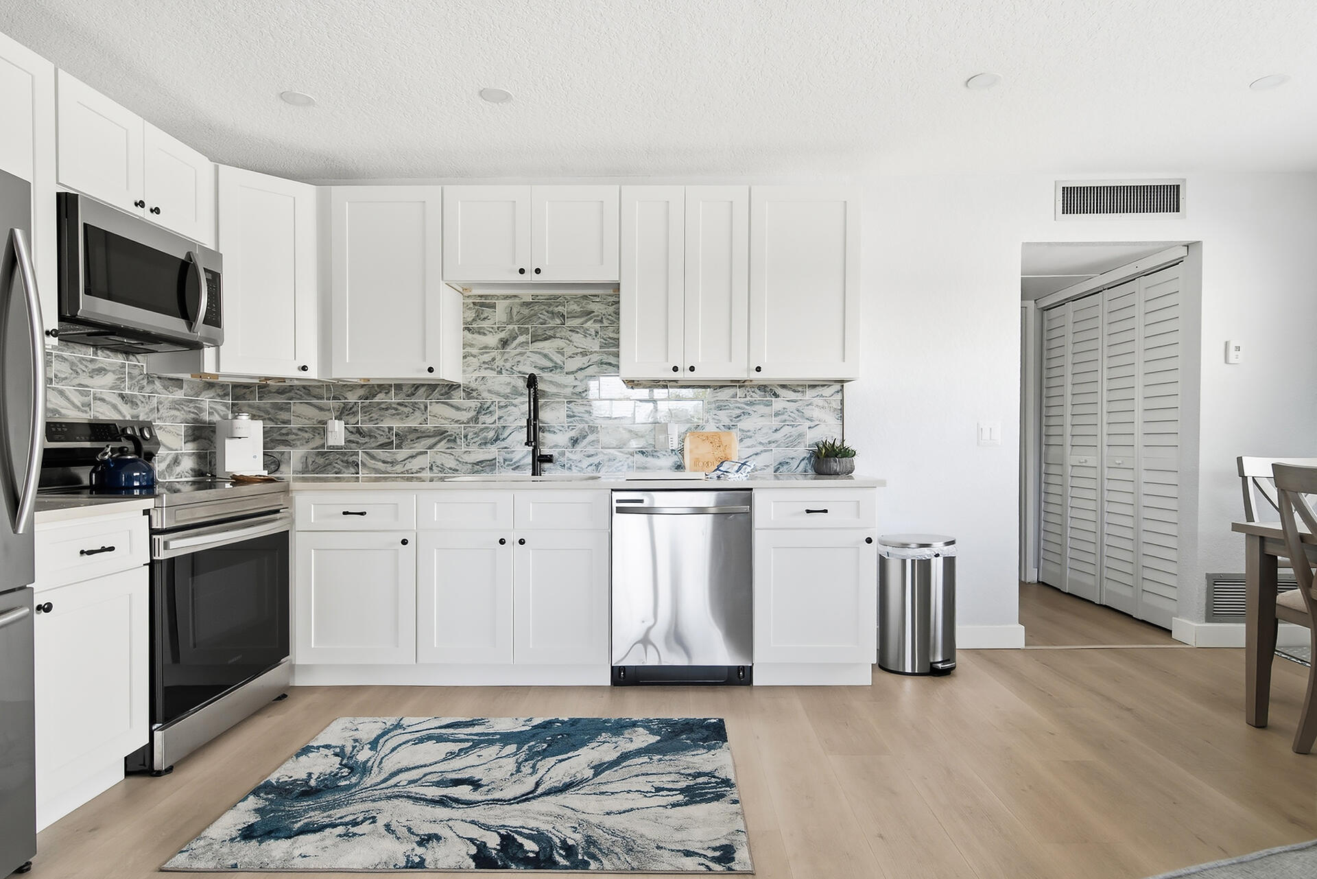 Kitchen with white cabinets, stainless steel appliances, and a blue-gray marbled tile backsplash.