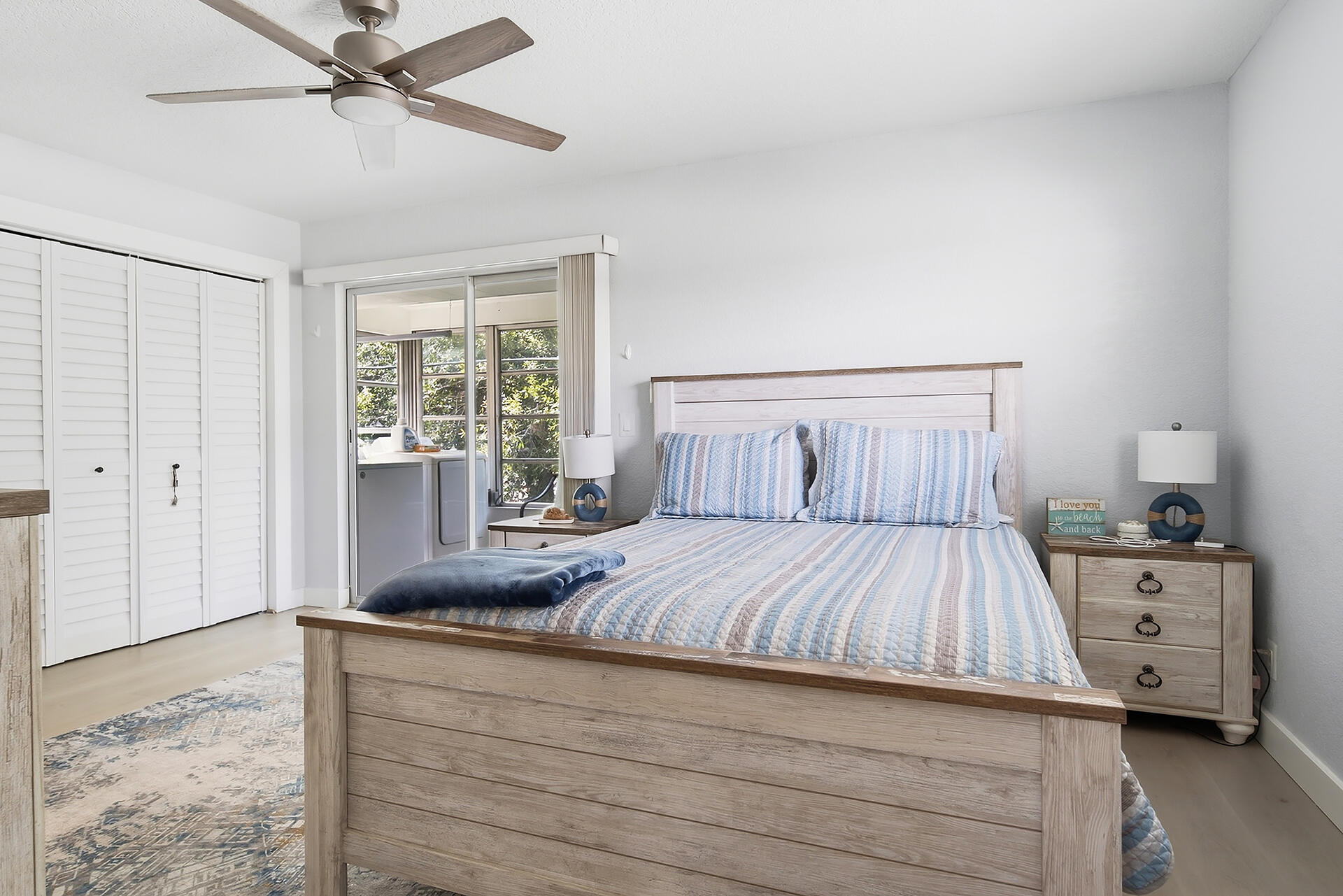 Furnished bedroom with blue striped bedding, a light wood bed, and sliding glass doors.