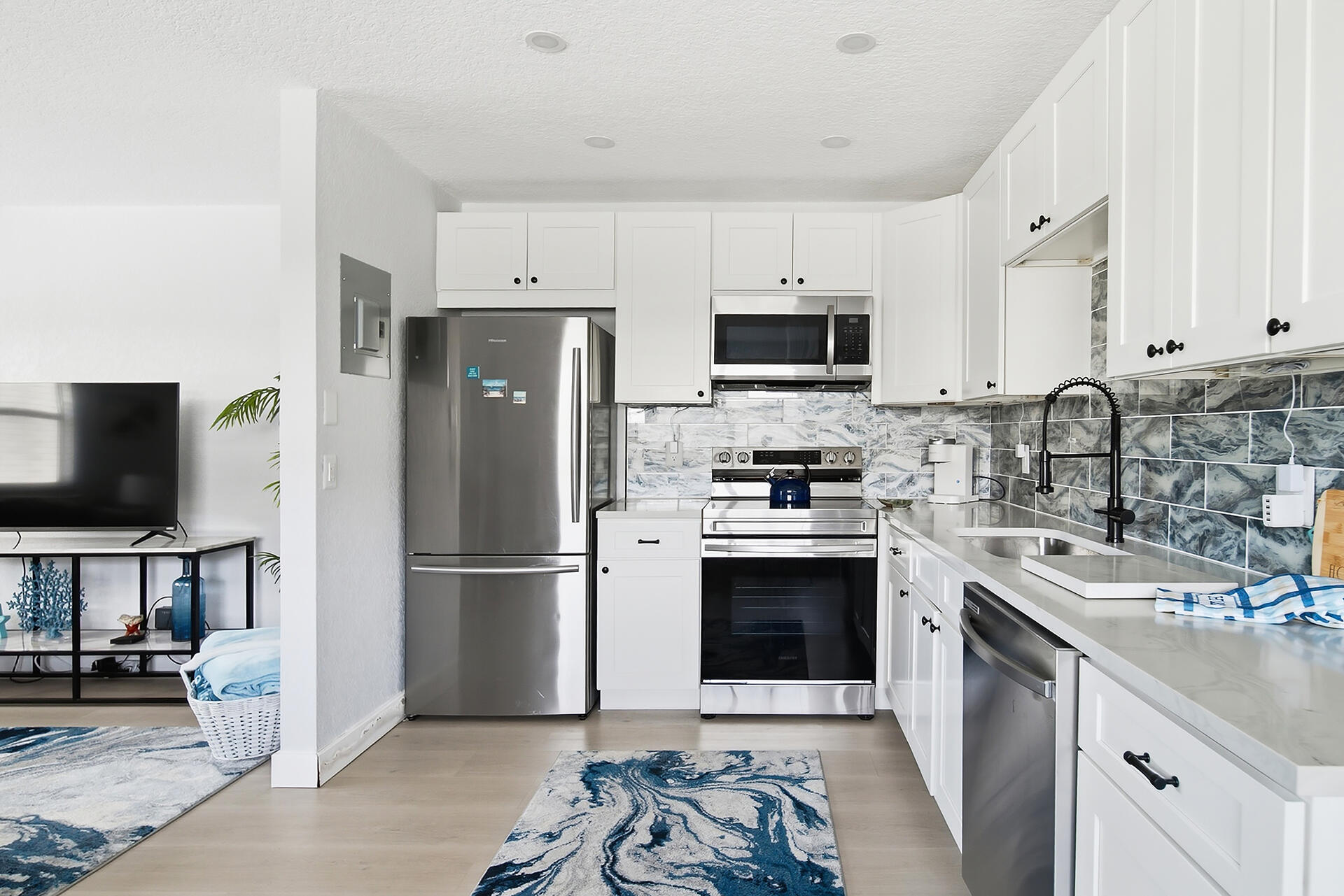Kitchen with white cabinets, stainless steel appliances, blue-gray tile backsplash, and black spring-coil faucet.