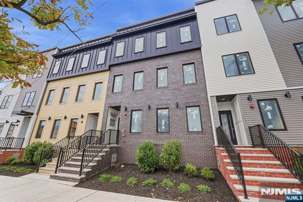 Modern multi-story building with brick steps, black railings, and landscaped shrubs.