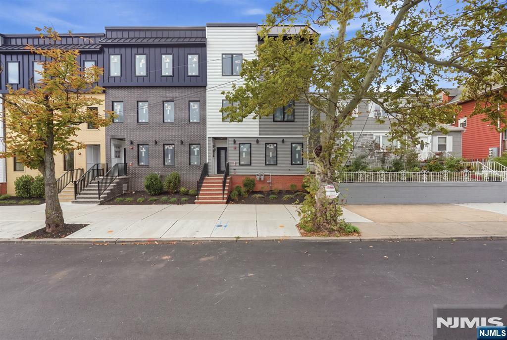 Modern three-story office building with dark brick, white siding, and autumn trees along the sidewalk.