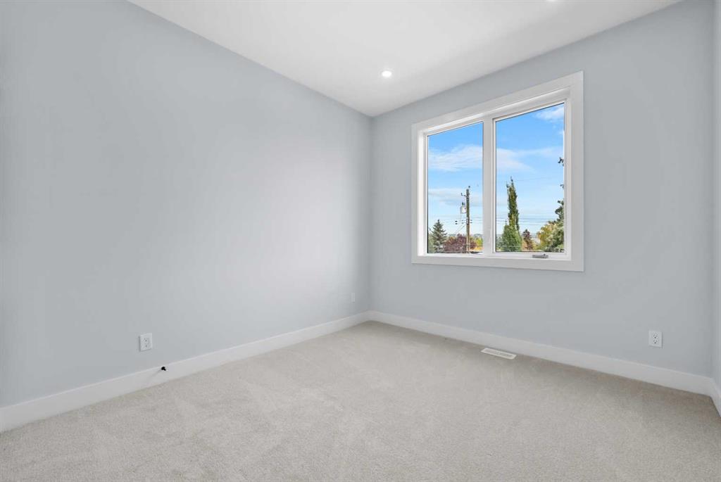 Empty carpeted room with pale gray walls and a window overlooking trees.
