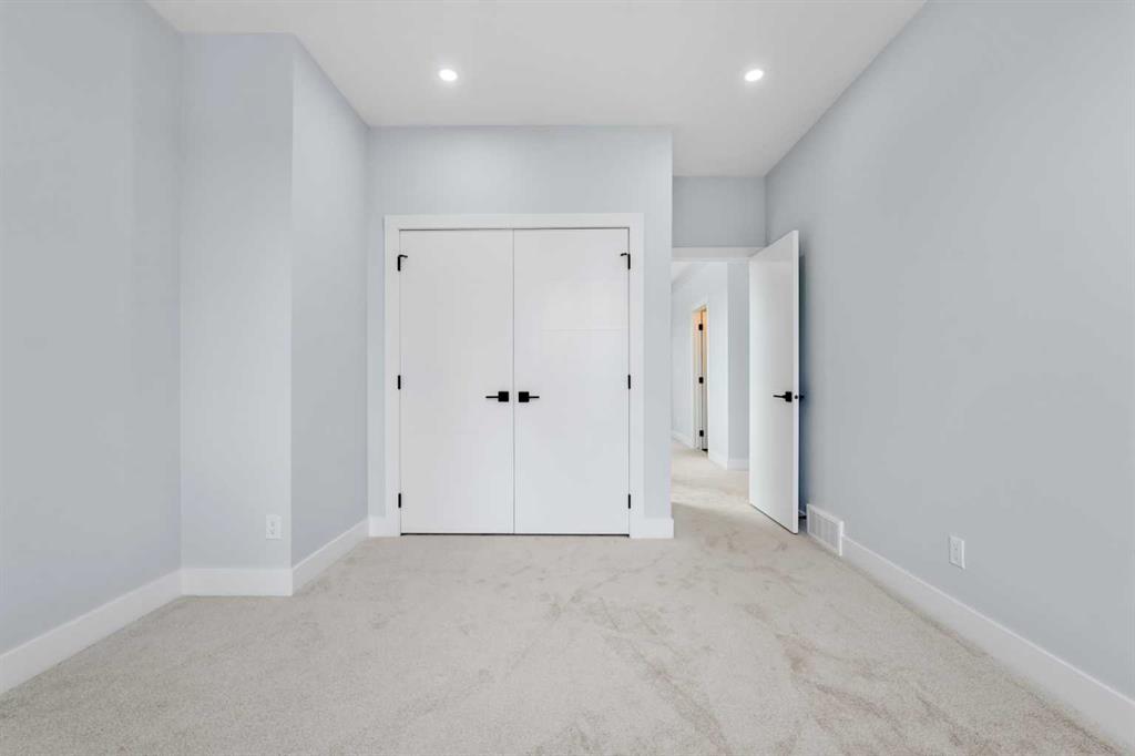 Empty bedroom with pale carpet, white double closet doors, and an open doorway.