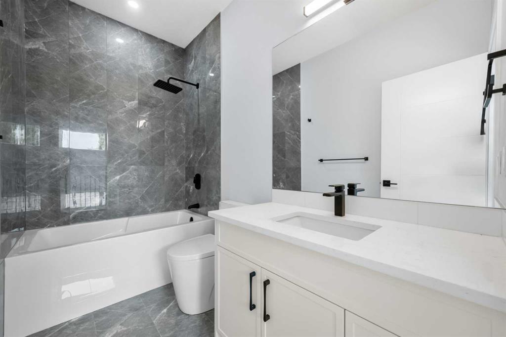 Bathroom with a white tub, dark gray marble-look tile, and a large vanity.