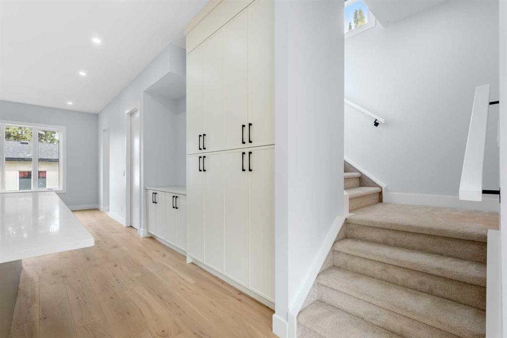 Bright kitchen with tall white cabinets and a carpeted staircase beside light wood flooring.