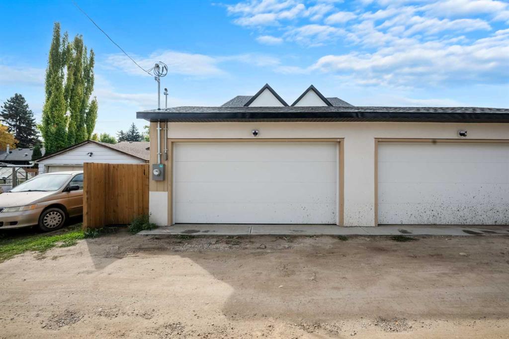 Cream-colored garage with two white doors beside a wooden fence and gravel driveway.