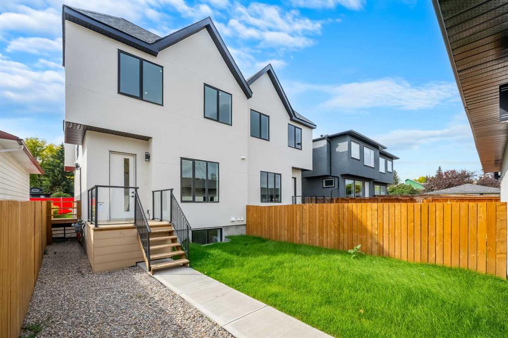 Modern white home with raised deck and stairs overlooking a fenced green backyard.
