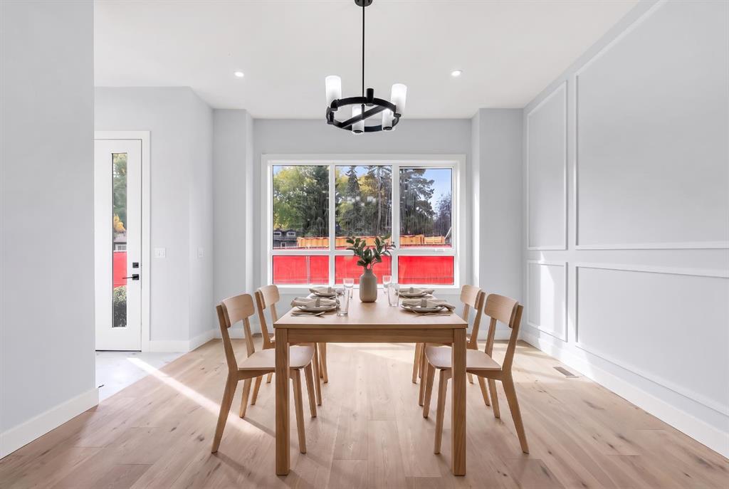 Staged dining room with a wooden table, black chandelier, paneled walls, and large windows.