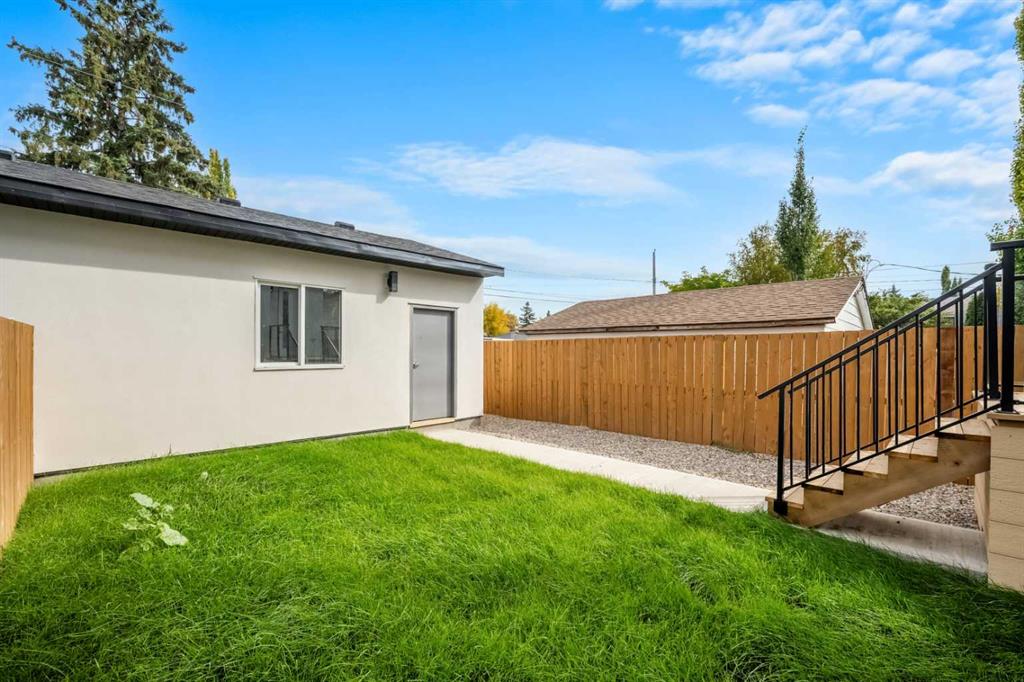 Backyard with a green lawn, wooden privacy fence, and black-railed stairs beside a white exterior wall.
