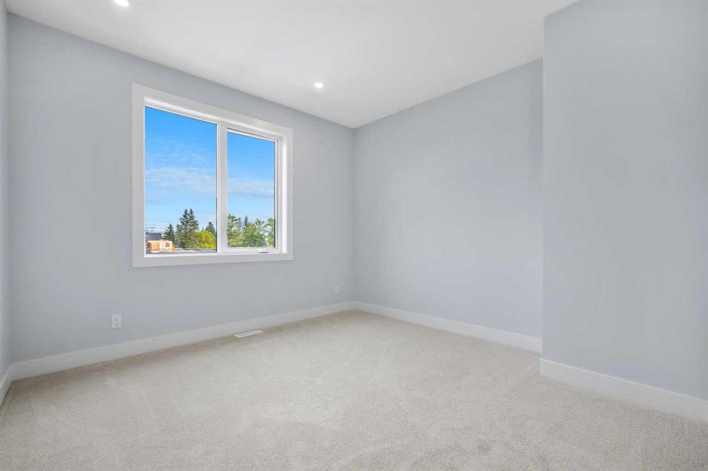 Empty bedroom with pale carpet, gray walls, and a large window overlooking trees.