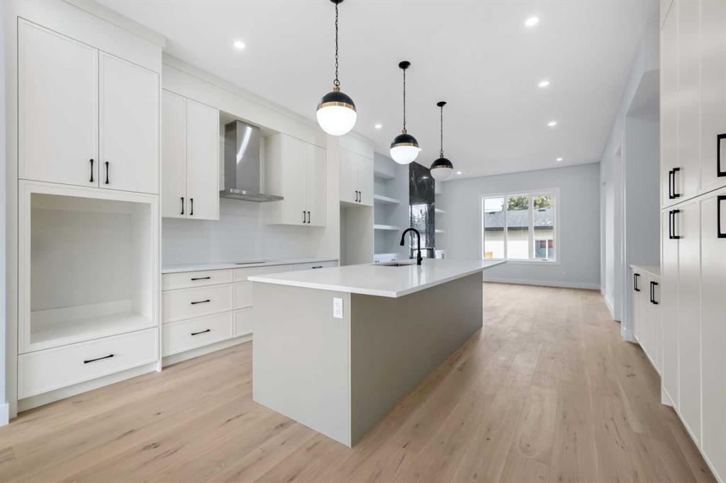 Modern white kitchen with a large island, light wood floors, and three pendant lights.