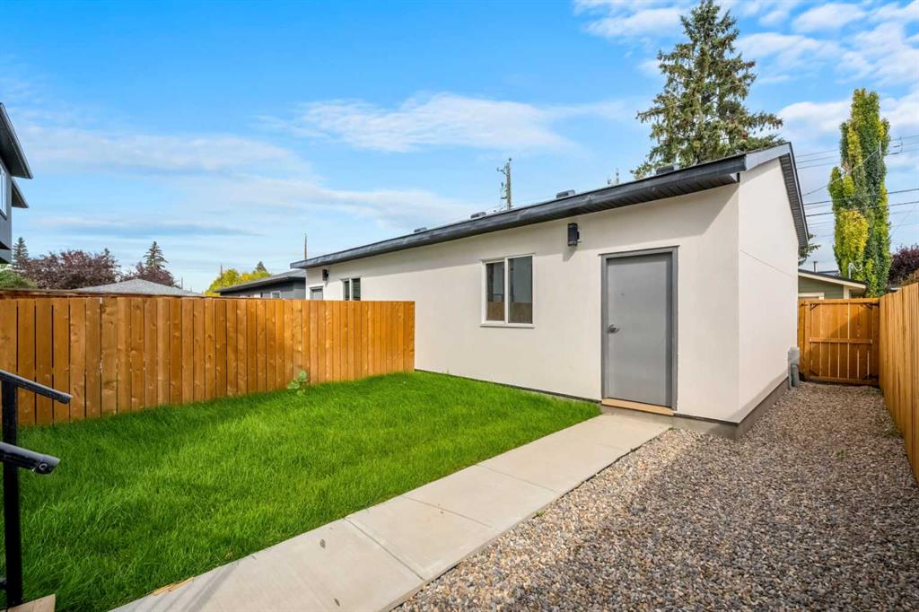 White single-storey structure beside a fenced lawn, with a concrete path and gravel side yard.