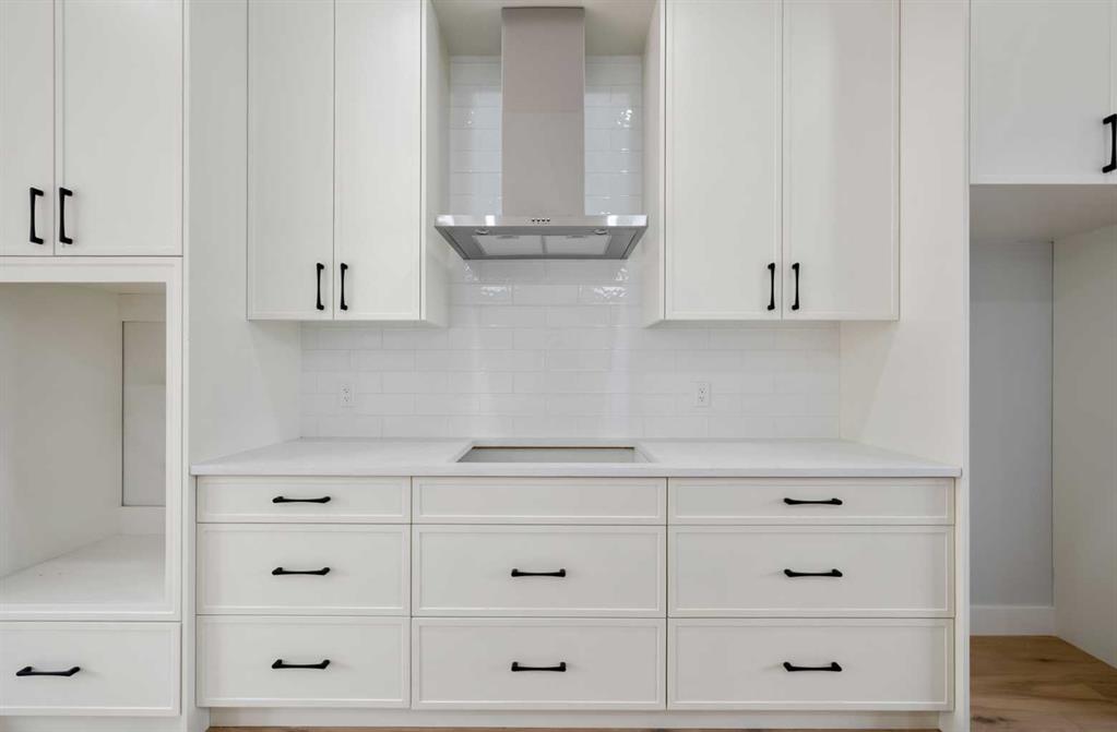 White kitchen cabinetry with black pulls, tile backsplash, and stainless-steel range hood.