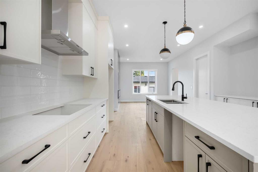 Modern white kitchen with a long island, black faucet and pale wood flooring.