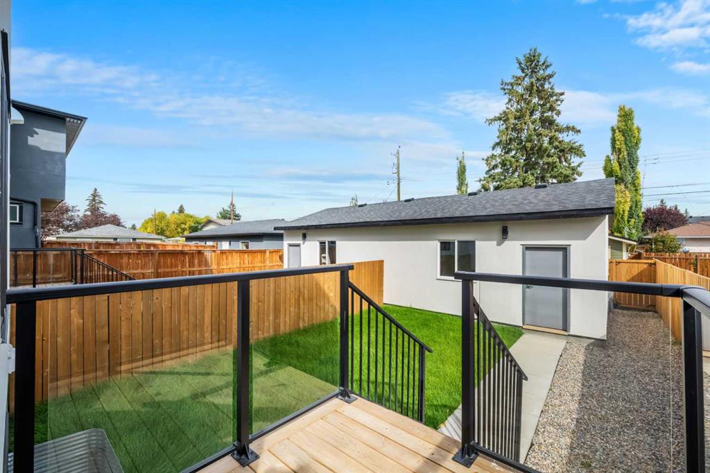 Home’s backyard with a raised deck, glass-and-metal railing, lawn, wooden fence, and gravel path.