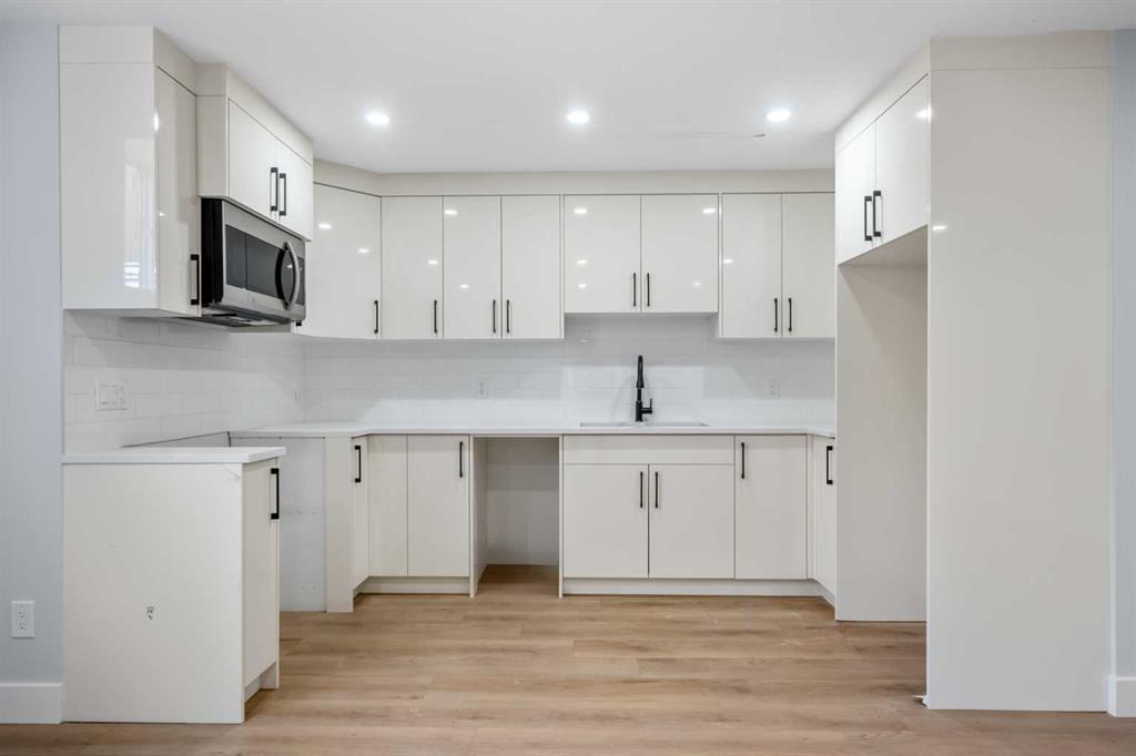Modern kitchen with white cabinets, tile backsplash, and light wood flooring.