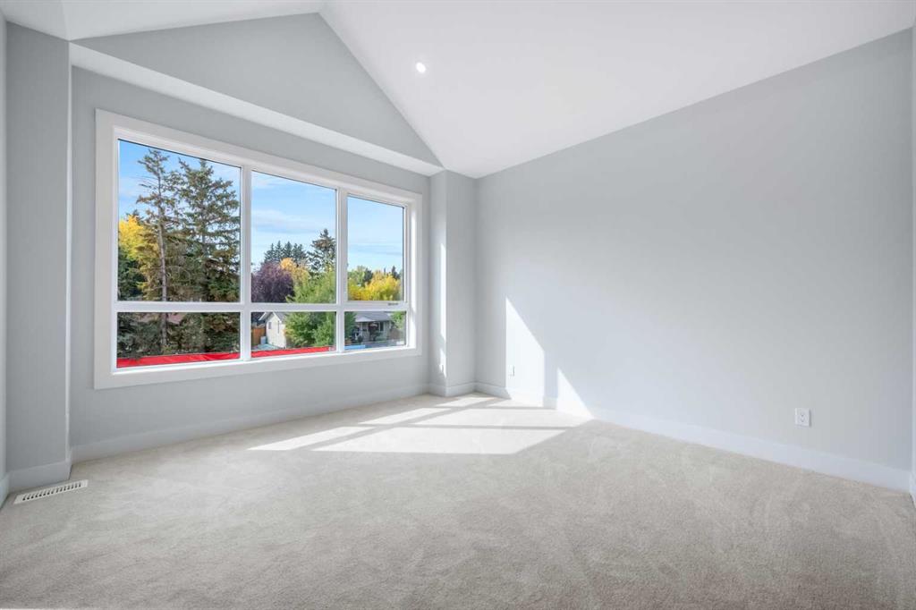 Empty bedroom with vaulted ceiling, large multi-pane window, and neutral carpet.