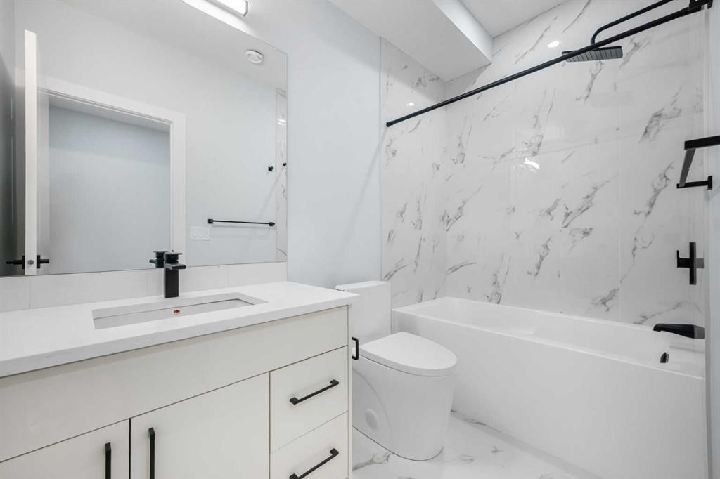 Modern bathroom with marble-look tile, a white bathtub, and a vanity with black fixtures.