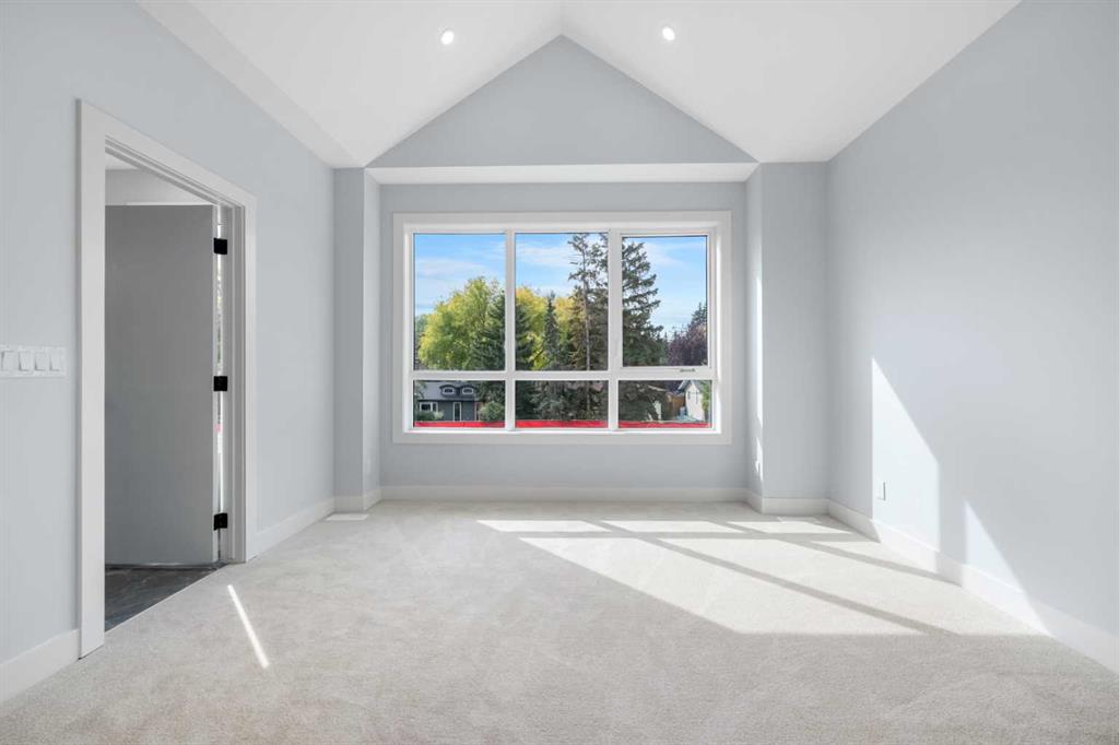 Vacant carpeted room with a peaked ceiling and large window overlooking trees.