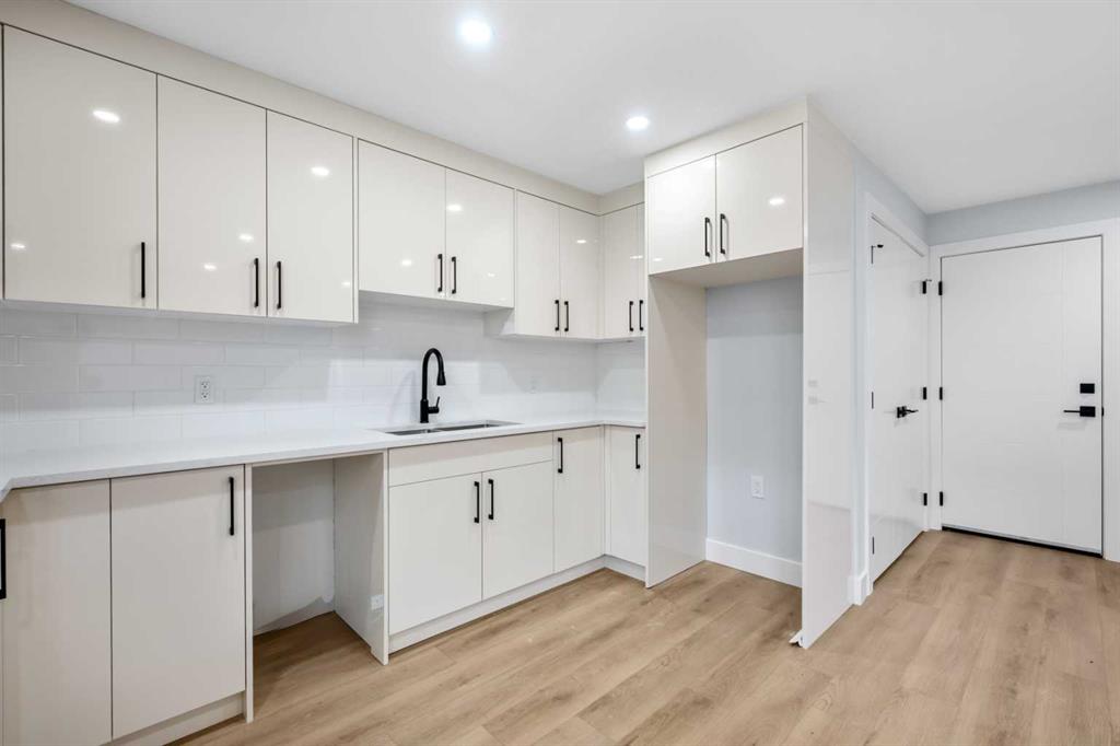 Vacant kitchen with white cabinetry, a black faucet, and light wood flooring.
