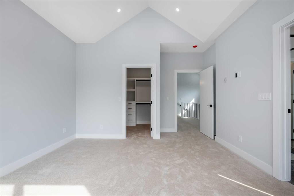 Unfurnished bedroom with a vaulted ceiling, carpet, and an open closet with built-in drawers.