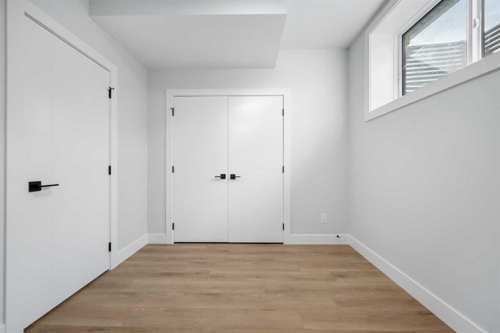 Empty room with light wood floors, a high window, and white doors with black hardware.