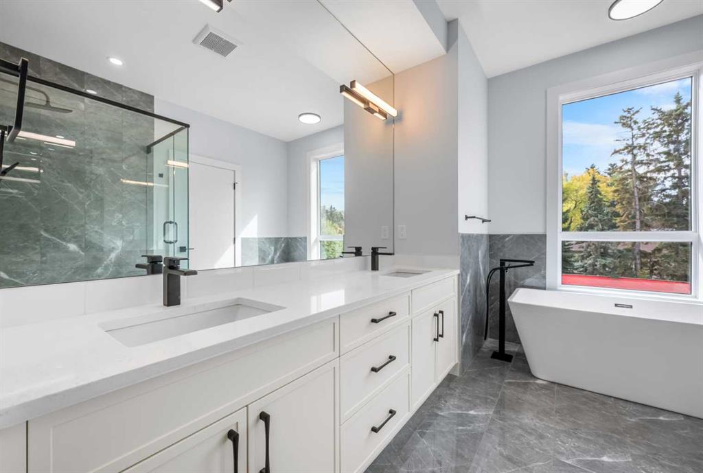 Modern bathroom with a white double vanity, glass shower, and freestanding tub by a large window.