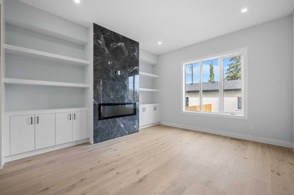 Vacant living room with pale wood floors, built-in shelving, and a dark fireplace feature wall.
