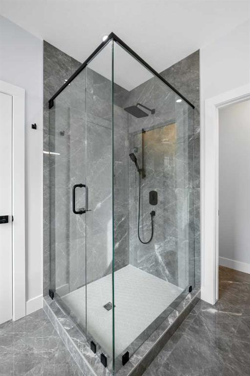 Glass-enclosed walk-in shower with gray marble-look tile and black fixtures.