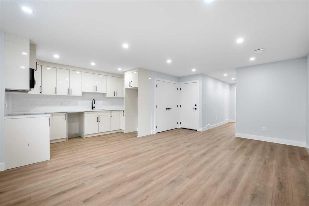Unfurnished open-plan kitchen and living area with white cabinets and light wood flooring.