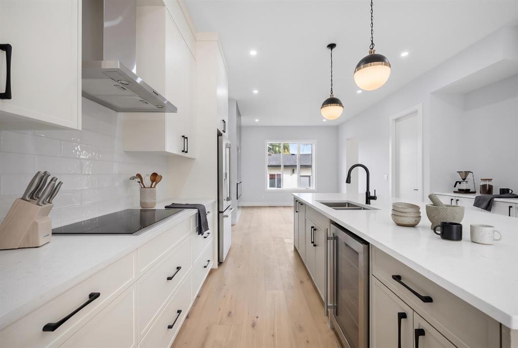 Modern white kitchen with a long island, black faucet, and pale wood floors.