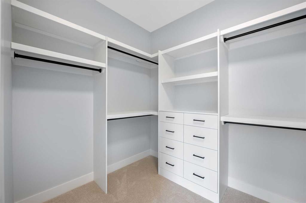 Walk-in closet with white built-in shelving, hanging rods, and a central bank of drawers.