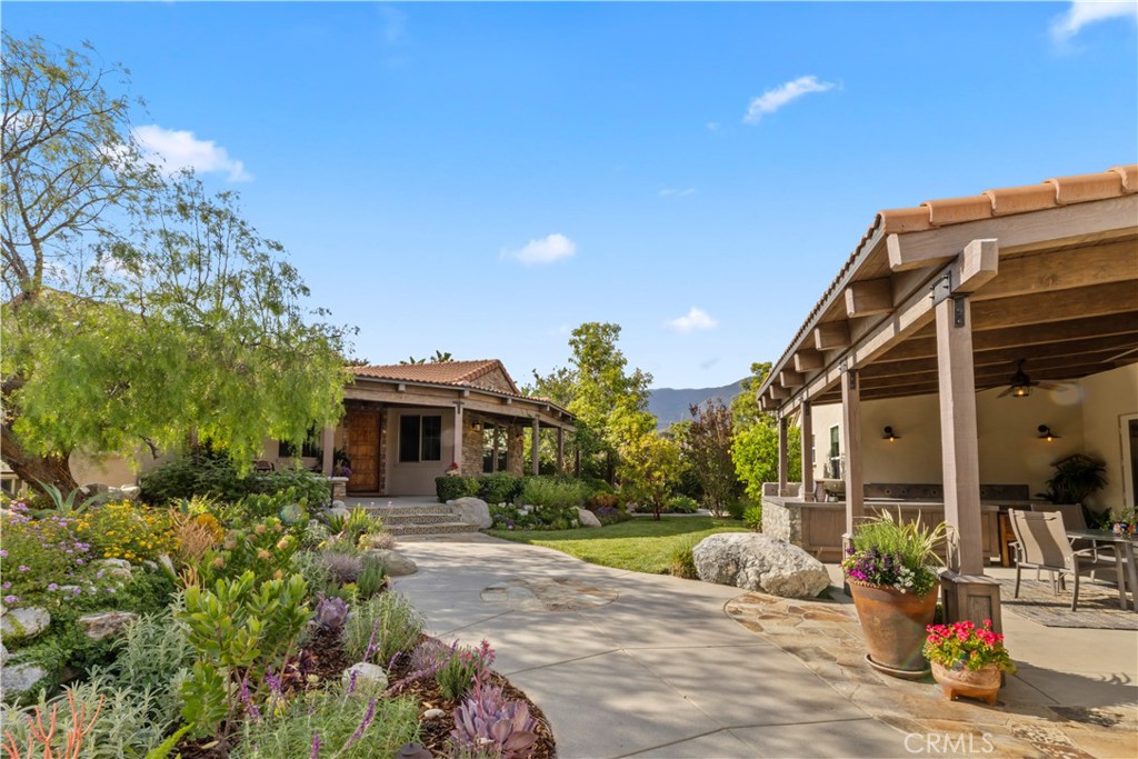 Home exterior with a flower-filled garden, curving walkway, and covered patio with outdoor seating.