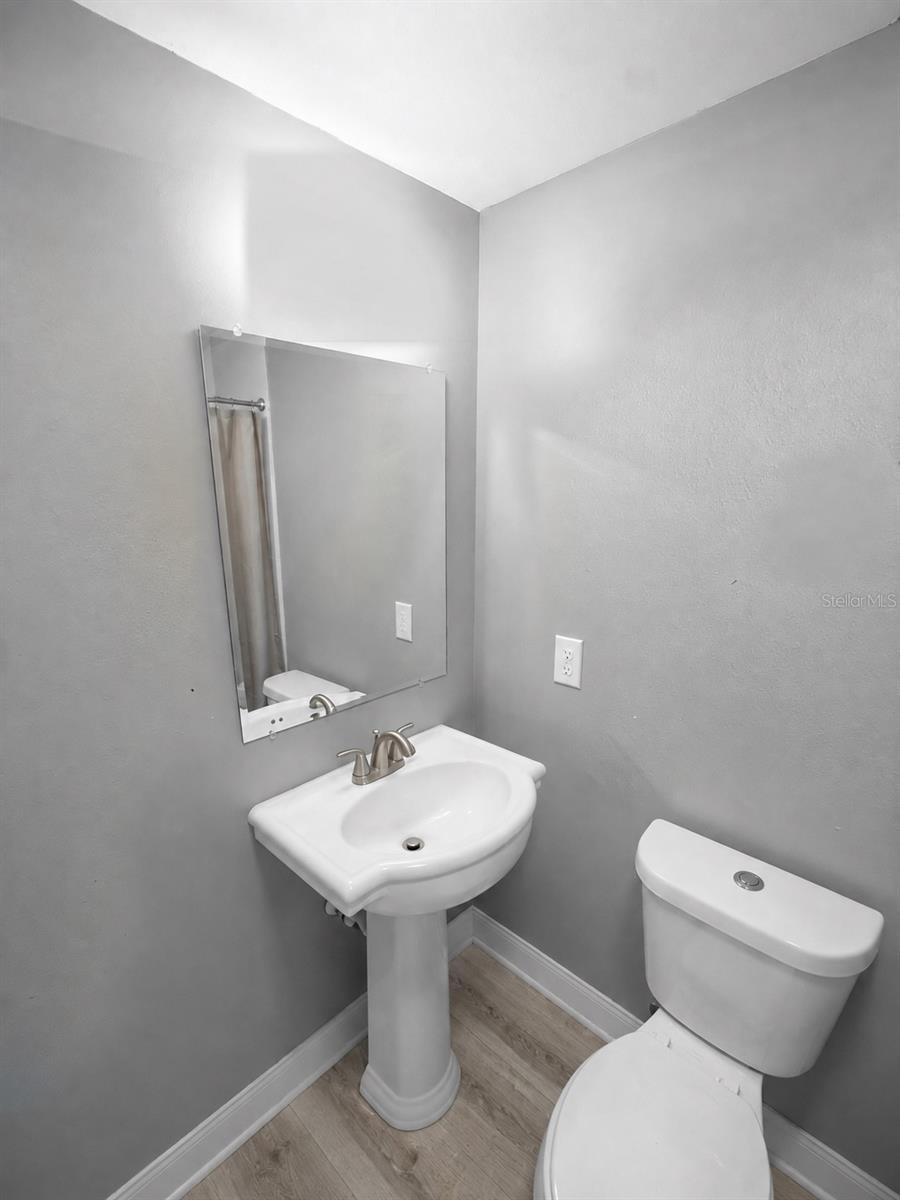 Compact bathroom with a pedestal sink, large mirror, toilet, and light wood-look flooring.