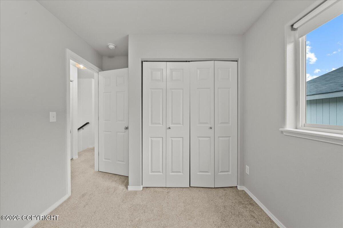 Vacant bedroom with a wide double closet, beige carpet, and a window overlooking a neighboring building.