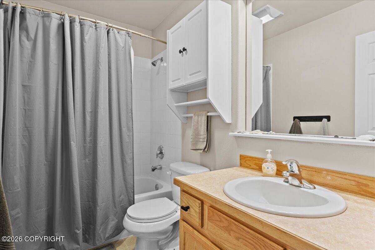 Bathroom with gray shower curtain, toilet, and wood vanity with oval sink.