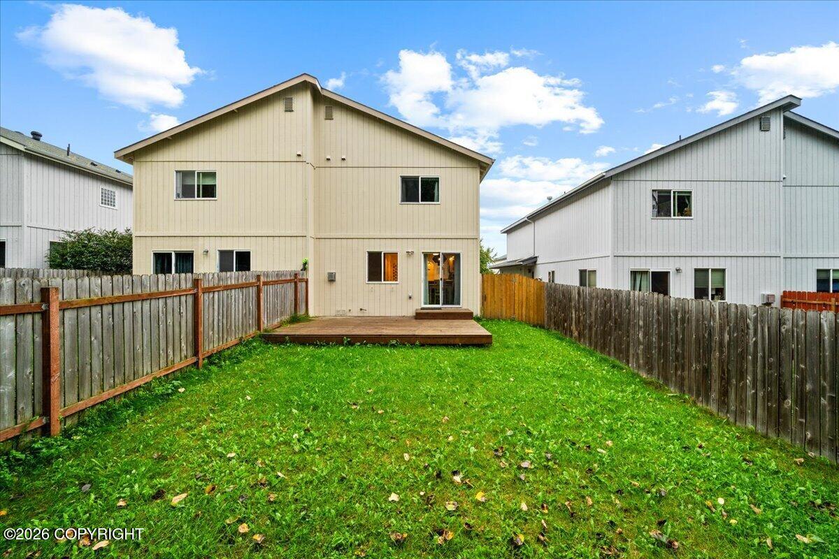 Rear of a beige two-story home with a small deck and fenced grassy backyard.