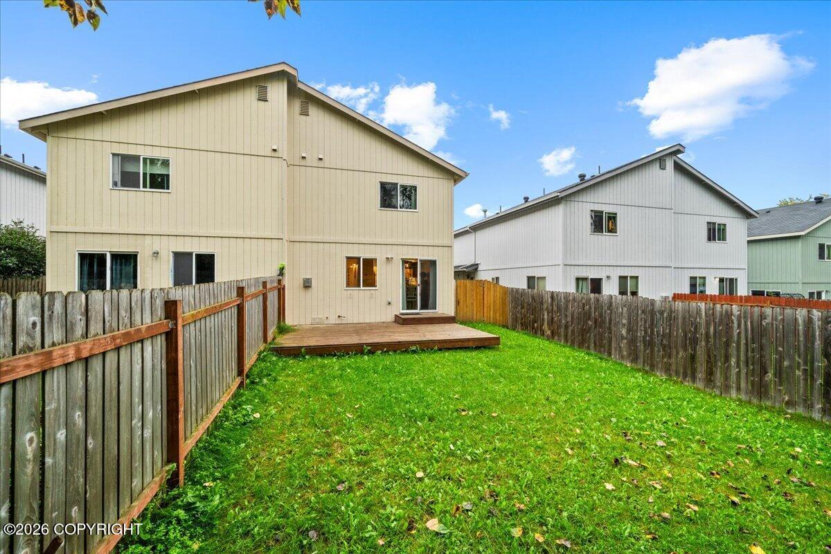 Rear of a beige two-story home with a fenced grassy backyard and small deck.