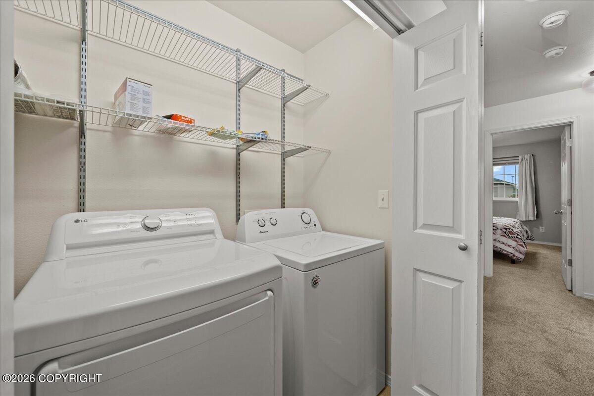 Laundry room with white washer and dryer, wire shelves, and an open doorway to a bedroom.
